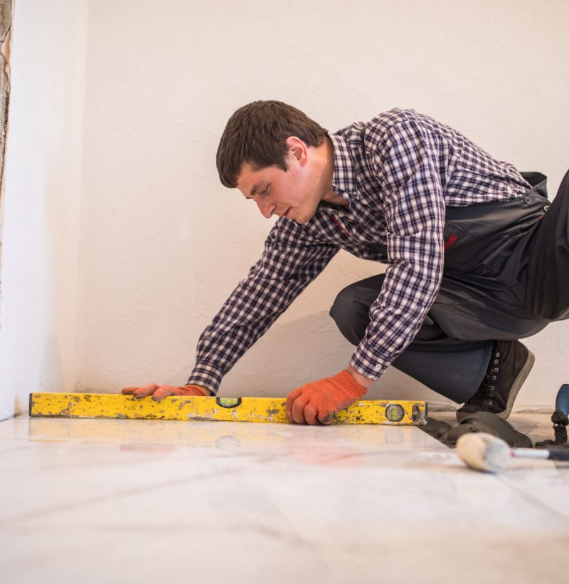 Home tile improvement - handyman with level laying down tile floor