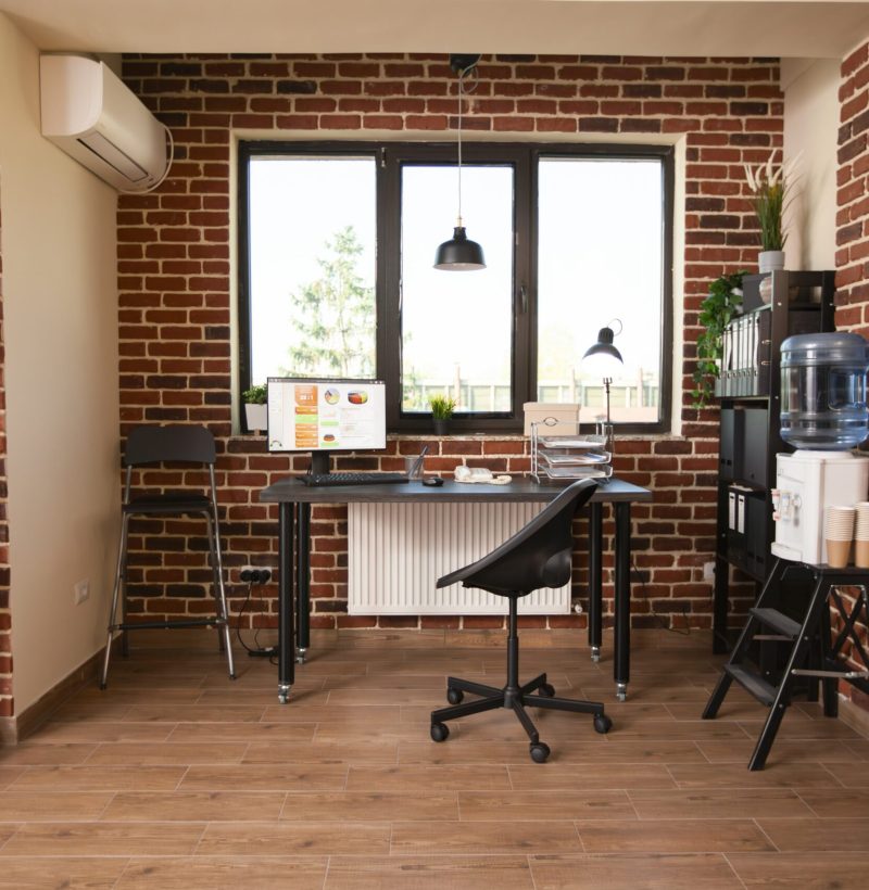 Vacant desk with desktop monitor showing financial analysis and marketing strategy charts. Spacious office with no people is neatly arranged with shelves, indoor plants, water cooler and computer.