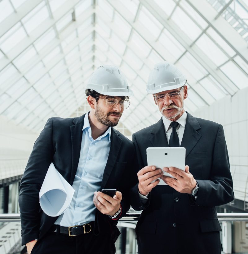 Two successful entrepreneur in helmet with project and laptop of new buildings stay near glass roof.